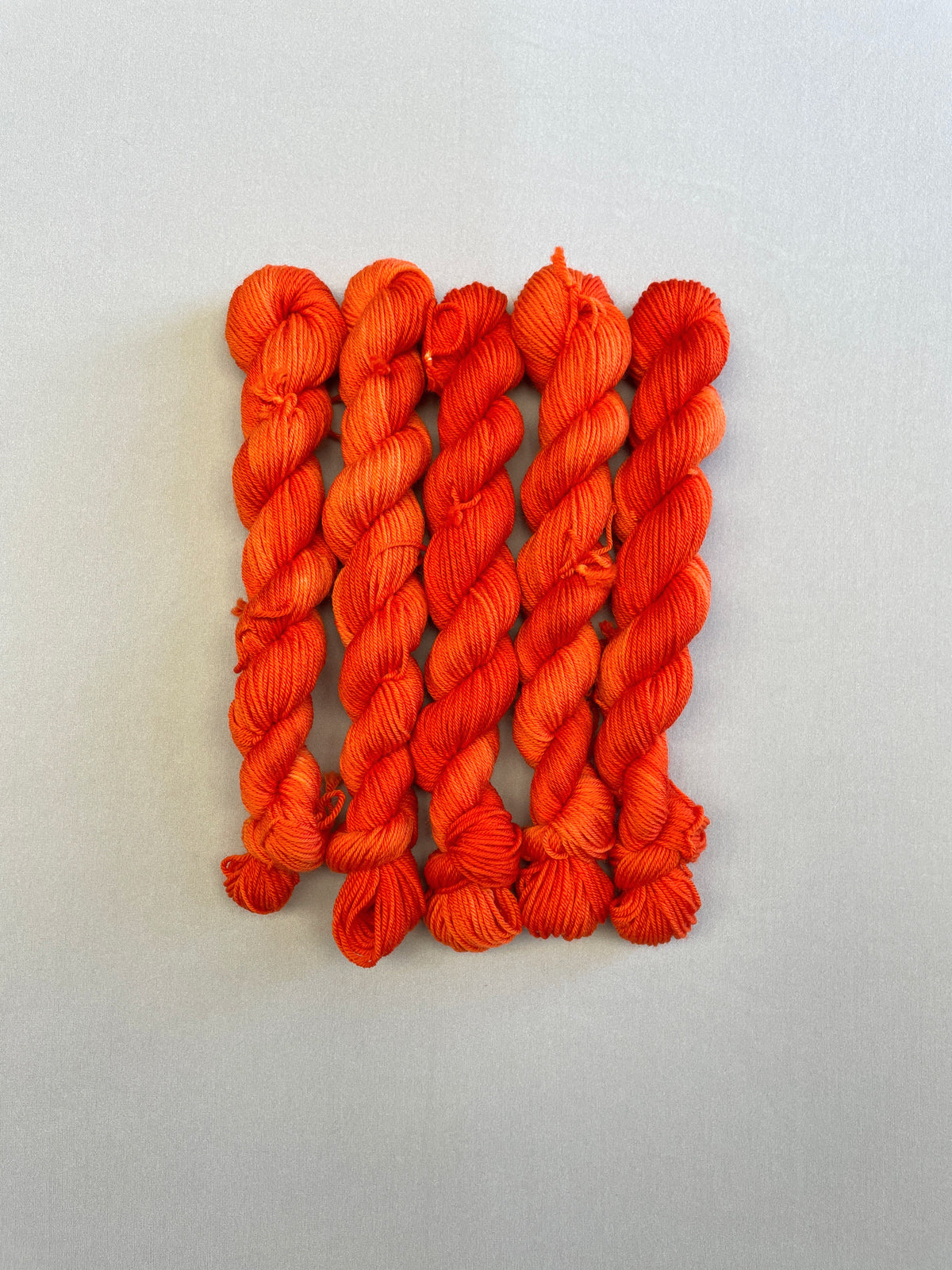 Full shot of Sock weight mini skeins in colourway Lava. This semi-solid colourway is dyed up in a bright, intense orange.